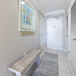 Welcoming entryway featuring a rustic bench, colorful artwork, and a cheerful sign inviting guests to relax