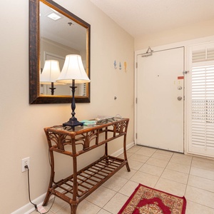 Welcoming entryway featuring a decorative mirror, a stylish lamp, and a wicker console table with a vibrant area rug
