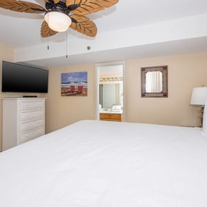 Master bedroom featuring a large TV, plush bedding, and a view into a stylish bathroom