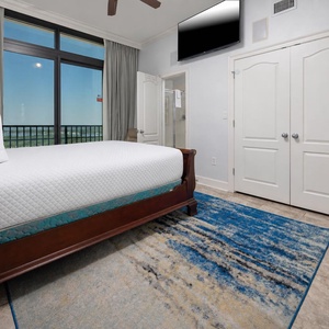 This bedroom features a plush queen bed, a large window with a stunning beach view, and a mounted TV for entertainment