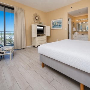 The bright master bedroom features a cozy seating area, a TV for entertainment, and a lovely view from the large window