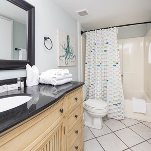 This bath features a stylish black granite countertop, a colorful fish-patterned shower curtain, and neatly arranged towels
