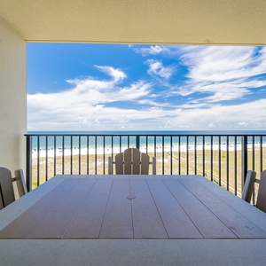 Balcony with a table and chairs offers a serene view of the beach, inviting relaxation and enjoyment of the gulf breeze