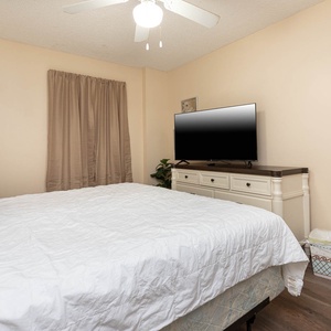 This bedroom features a comfortable king bed, a large TV for entertainment, and soft beige tones for a calming atmosphere