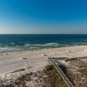 A serene view showcases a wide stretch of white sand beach with gentle waves and beachgoers enjoying the sun and surf