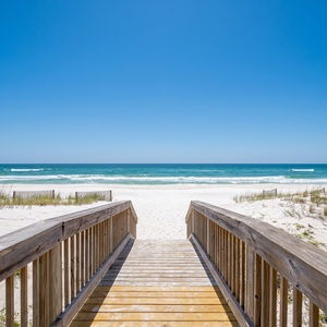 Step onto the wooden walkway leading to the beach, where colorful umbrellas and sunbathers await your arrival to Sea Glass