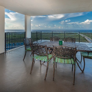 Spacious extended balcony with a dining table and chairs offers a serene view of the beach and lush greenery beyond