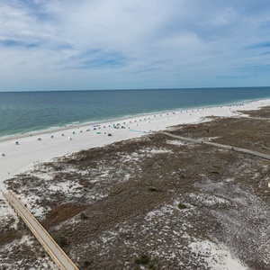 Expansive view of the beach with white sand and turquoise umbrellas, framed by lush greenery and the inviting pool area