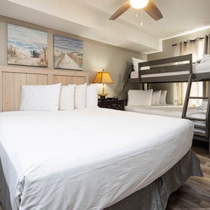 Guest bedroom featuring a queen bed with multiple pillows, a twin over full bunk bed, and beach artwork on the walls