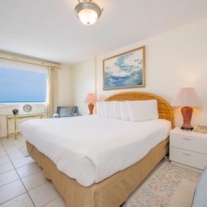 This bedroom features a large bed, elegant decor, and a stunning beachfront view through the expansive window