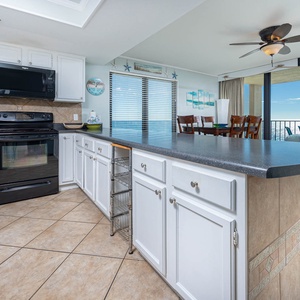 This kitchen features sleek black and stainless appliances, a spacious countertop, and a lovely view of the beach