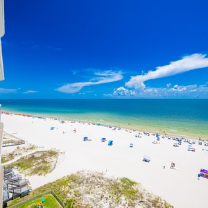 The stunning view from the balcony showcases a beautiful beach with white sand and colorful umbrellas, perfect for relaxation