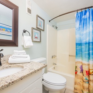 The bathroom features a stylish granite countertop, a colorful beach-themed shower curtain, and fresh towels for your comfort