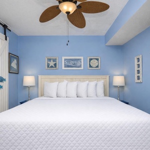 The master bedroom features a cozy king bed with decorative beach-themed accents and a soothing blue color scheme