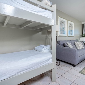 A cozy nook features a twin bunk bed and a sofa with queen sleeper, complemented by beach views through sliding glass doors