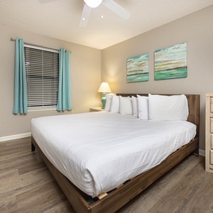 Brightly decorated guest bedroom featuring a king bed, soft linens, and coastal artwork, complemented by natural light