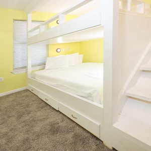 Yellow walls complement a cozy guest room featuring two queen bunk beds and a staircase leading to an upper sleeping loft