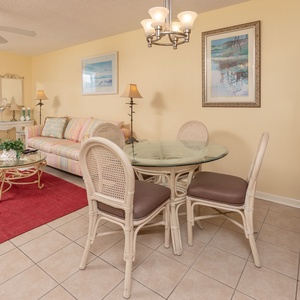 Cozy living area features a striped sofa with queen sleeper, glass dining table, and views of the beach through large windows