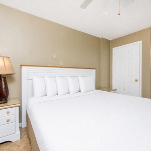 The master bedroom features a large bed with plush pillows, a stylish lamp, and a peek into a bright bathroom