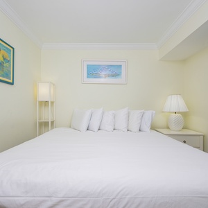 This inviting bedroom features a large bed with plush pillows, soft lighting, and cheerful artwork for a relaxing stay