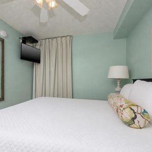 Relax in this tranquil bedroom featuring a king bed, a mounted TV, and soft colors for a restful atmosphere