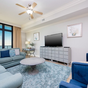 This inviting living area features plush blue seating, a large TV, and beachfront views through expansive windows