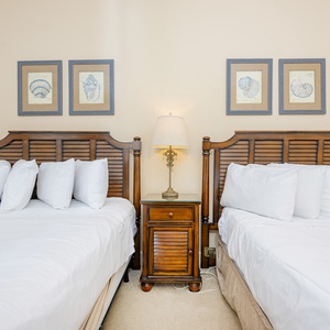 Cozy guest bedroom featuring two queen beds, decorative shell artwork, and a charming bedside lamp for a relaxing atmosphere