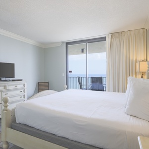 The master features a king bed, a TV, and access to a balcony with a serene view of the beach