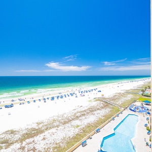 Breathtaking beachfront view showcases the sparkling blue water and white sand, with a pool area visible below