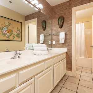 Brightly decorated master bath features a spacious double sink vanity, artistic wall decor, and a tub/shower combo