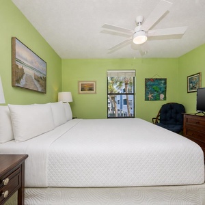 This bright bedroom features a king bed, a TV, and a view of palm trees through the window, perfect for relaxation