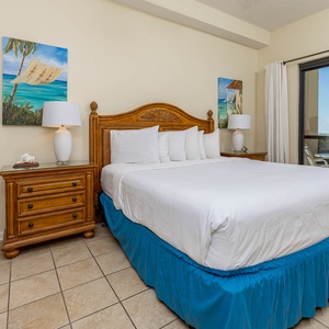 Brightly decorated master bedroom with a king bed and coastal artwork, leading to the outdoor patio seating area