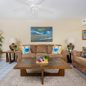 Living room features a cozy brown sofa with decorative pillows, a wooden coffee table, and a large TV against a light wall