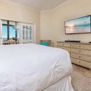 Master bedroom featuring a comfy king bed, a flat-screen TV, and a glimpse of the beautiful coastal view