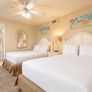 Guest room featuring two double beds, a cozy lamp, and beach artwork, creating a relaxed vacation atmosphere