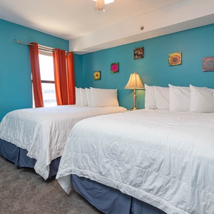 This bright guest bedroom features two full beds, bright blue walls, and cheerful artwork, perfect for a relaxing stay