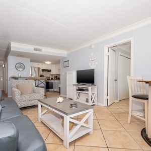 The space features comfortable seating, a TV, and a view of the adjacent kitchen, perfect for relaxation