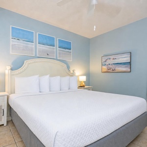 Cozy bedroom featuring a king bed, soft lighting from bedside lamps, and beach-themed artwork on the walls
