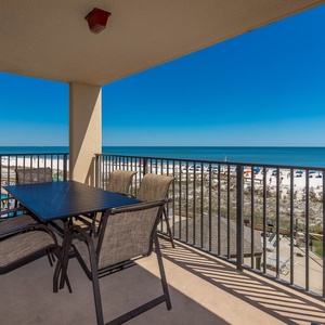 The balcony features a dining table with chairs, offering a serene view of the beach and the inviting blue waters