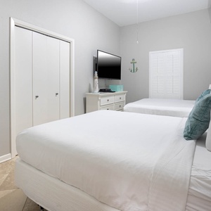 Guest bedroom featuring two queen beds, a TV, and coastal decor, creating a relaxed atmosphere for restful stays