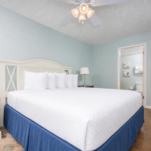 The serene guest bedroom features a large king bed with crisp white linens, a bedside lamp, and a view into the en-suite bath