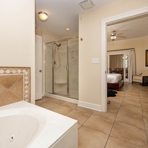 The master bathroom features a relaxing tub, a glass walk-in shower, and a view into the cozy bedroom area with elegant decor