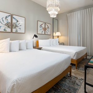 Relax in this inviting guest room featuring two plush queen beds, stylish decor, and art that enhances the coastal vibe