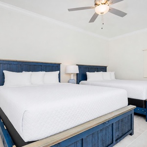 Rest comfortably in this inviting guest bedroom with two plush queen beds, stylish blue headboards, and soft lighting
