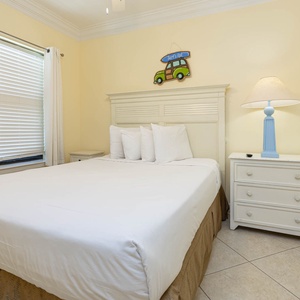 Cozy guest bedroom featuring a queen bed, light yellow walls, and a charming beach decor accentuated by a blue lamp