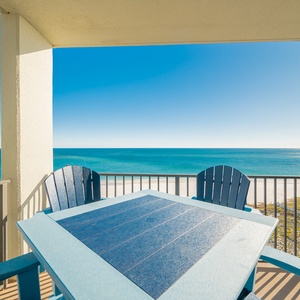 Balcony seating with blue chairs offers a serene view of the tranquil gulf waters and white sand beach below