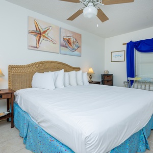 Inviting guest bedroom featuring a king-size bed, coastal artwork, and a charming seating area by the window