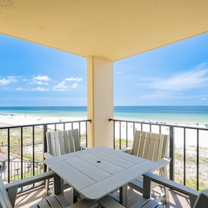 The balcony features a patio table and chairs, offering a clear view of the beach and vibrant blue waters beyond