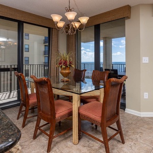 Dining area features a glass-top table with wicker chairs, offering a view of the gulf through expansive windows