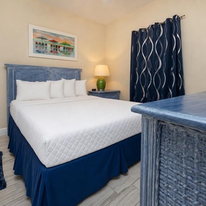 This cozy bedroom features a blue wicker bed frame, colorful artwork, and a TV for relaxing evenings